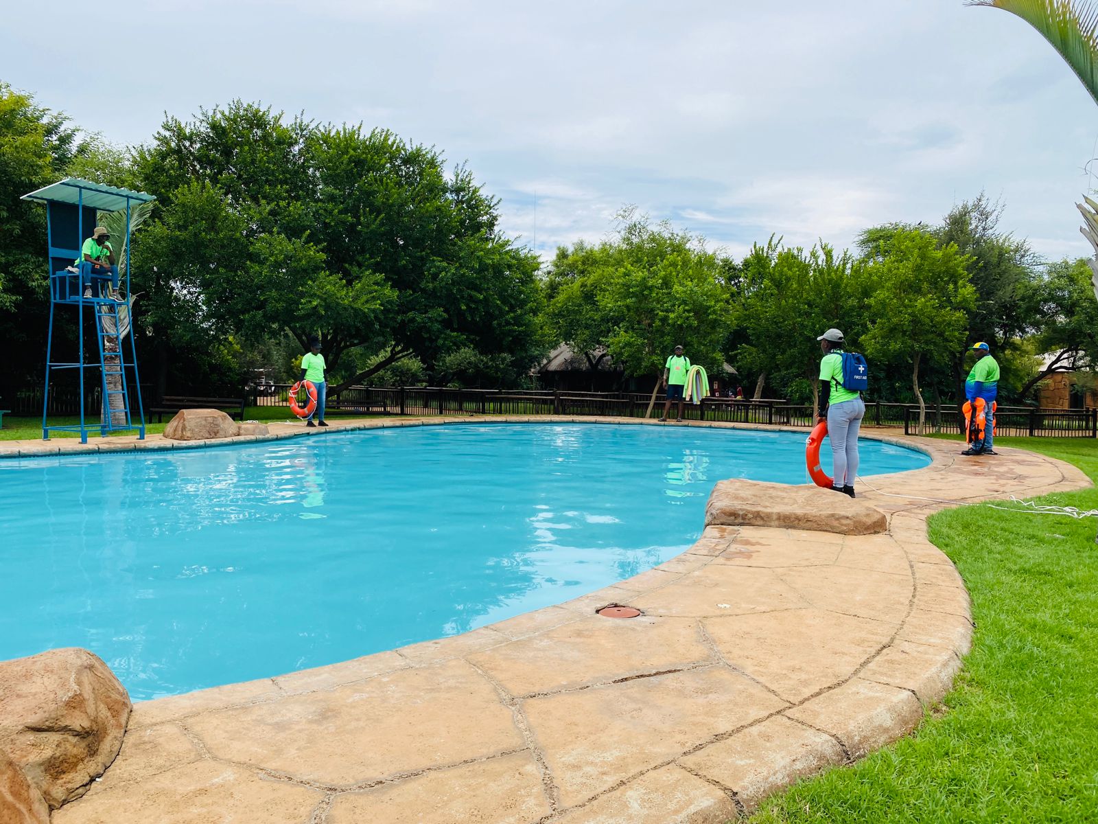 Water-safety facilitators positioned around a swimming pool with rescue equipment